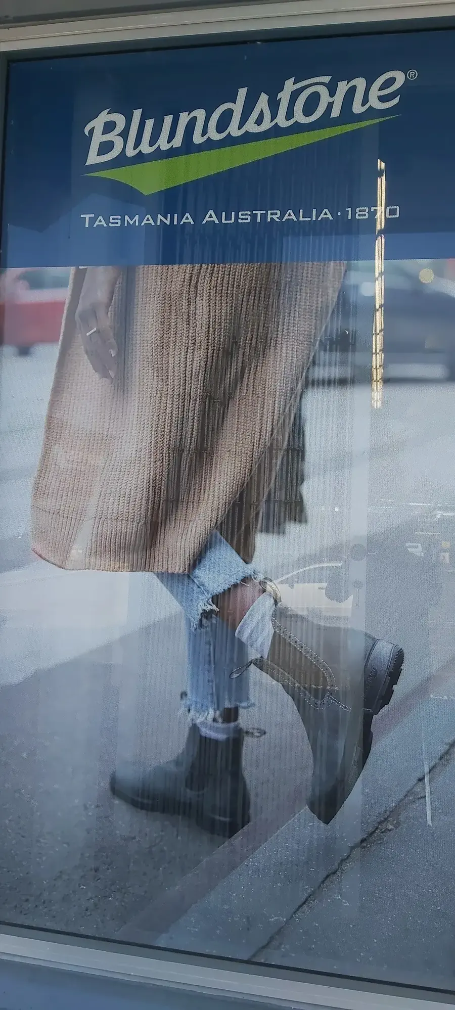 A Blundstone window poster showing a women's Chelsea boot worn with a long knit coat