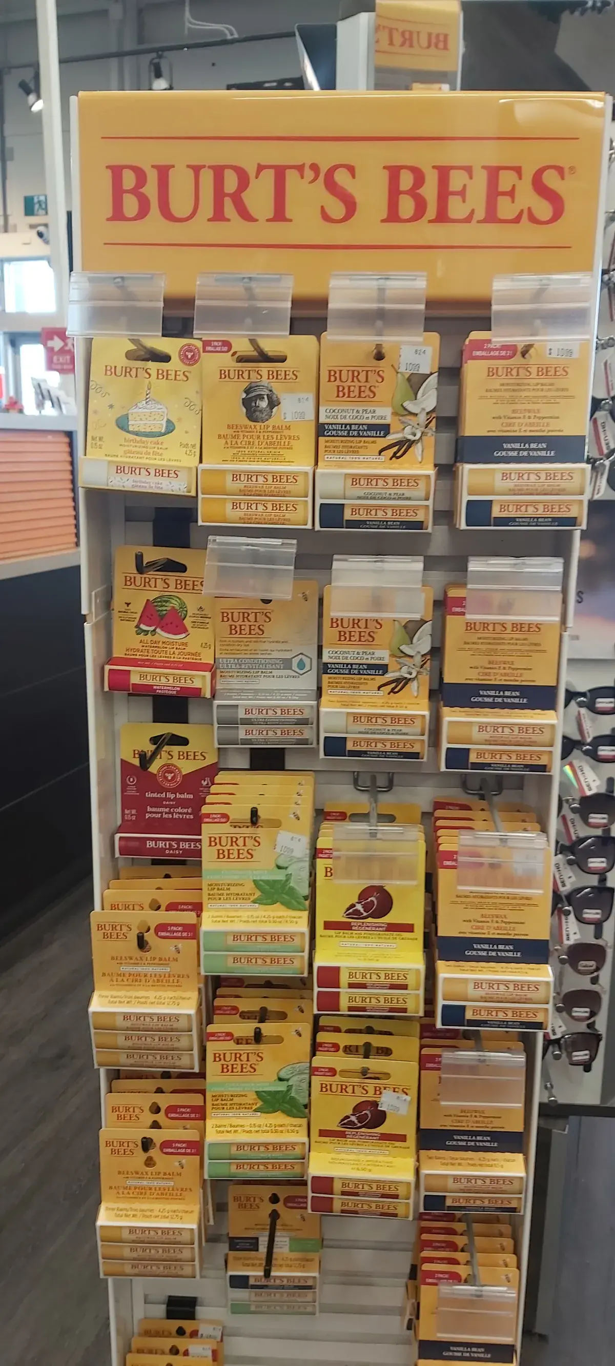 A Burt's Bees display stand of lip balms and hand salves under a yellow header