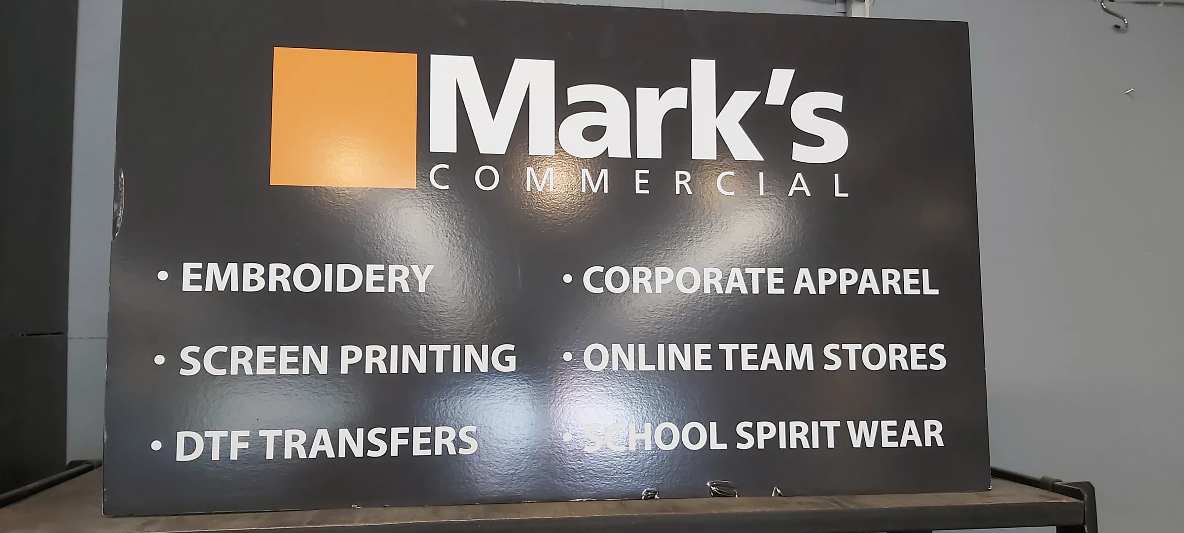 The Mark's Commercial department sign, listing embroidery, screen printing, DTF transfers, corporate apparel, online team stores and school spirit wear