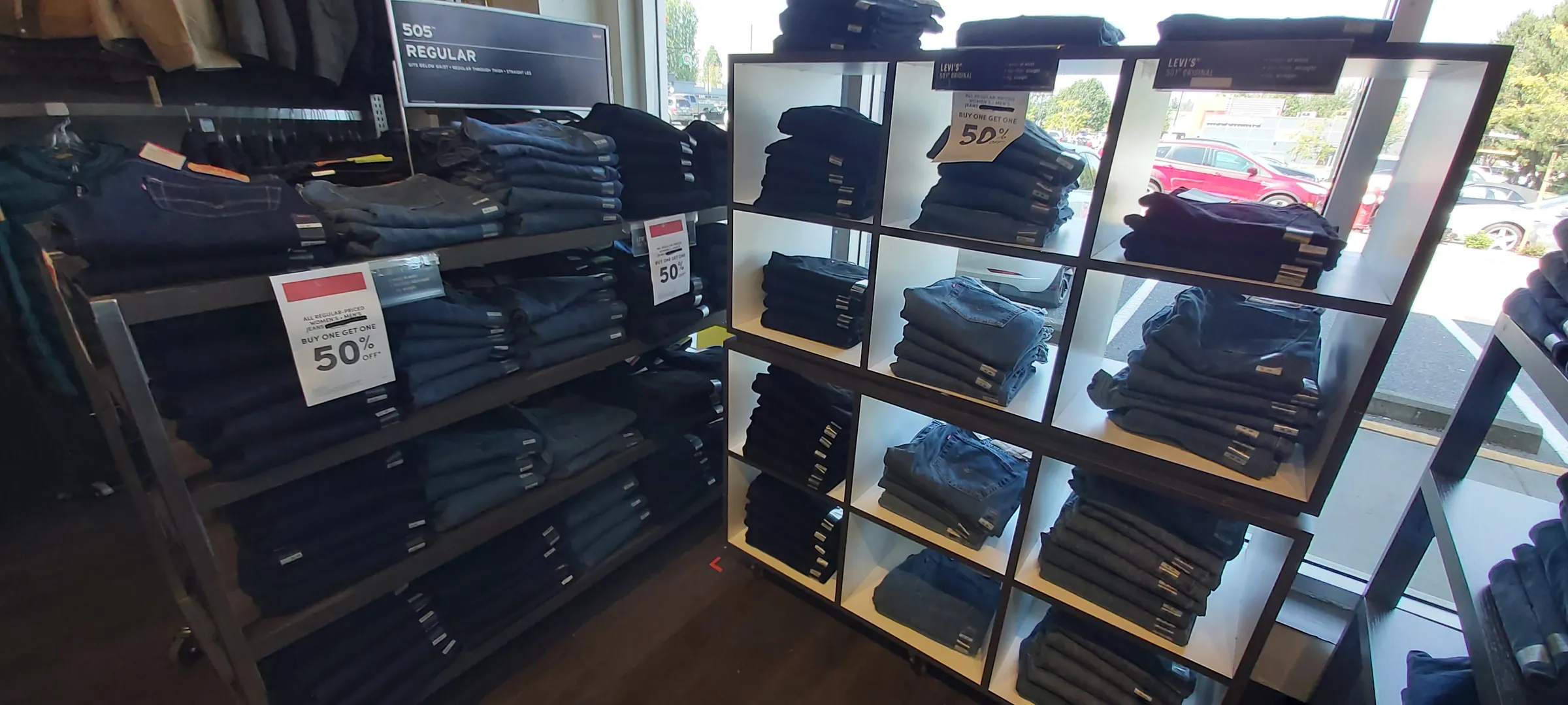 Folded denim in an open cubby fixture beside a jeans rack, with promotional signage