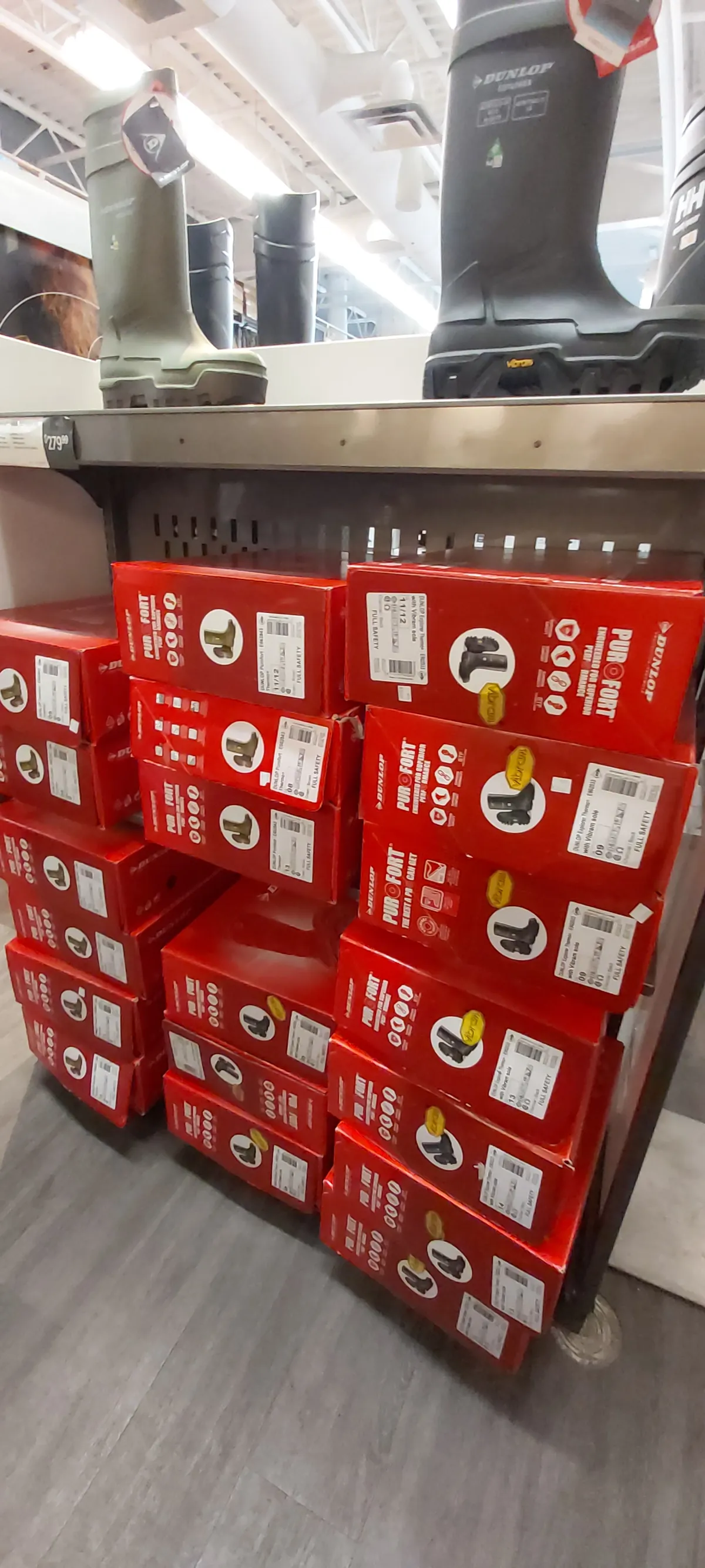 Dunlop Purofort rubber safety boots boxed on a pallet, with sample boots on the shelf above