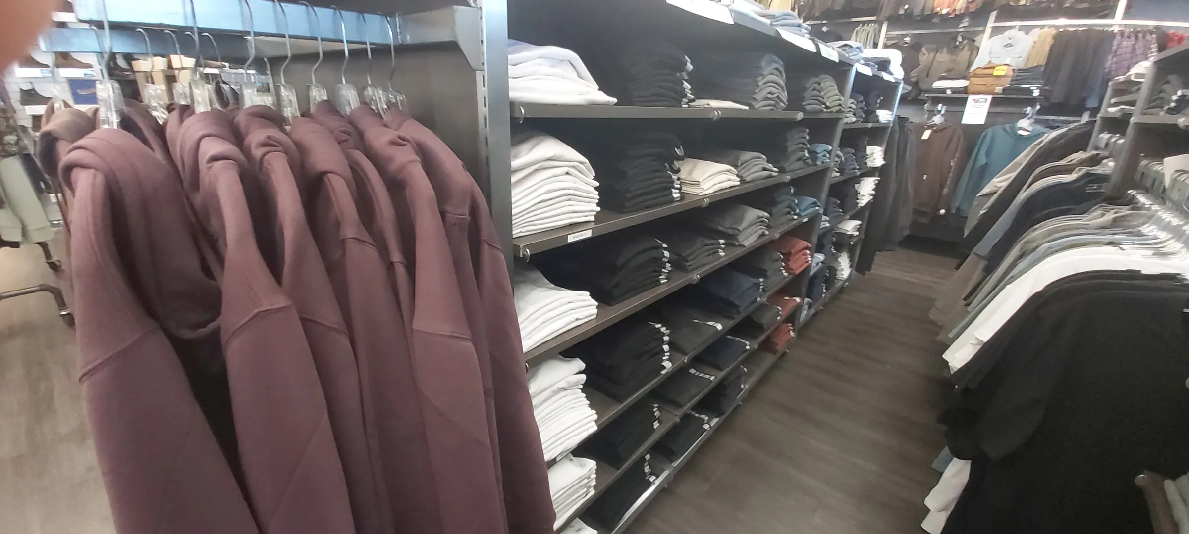 A rack of hooded sweatshirts beside folded stock on open shelving