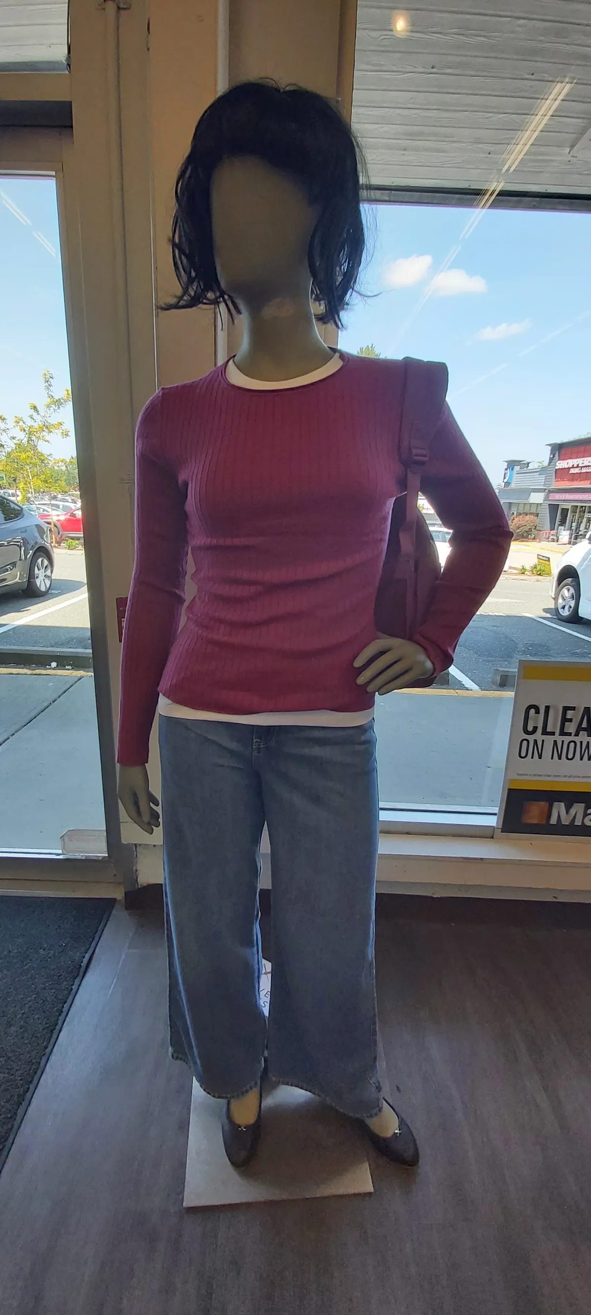 A women's mannequin in a pink knit top and wide-leg jeans by the front windows