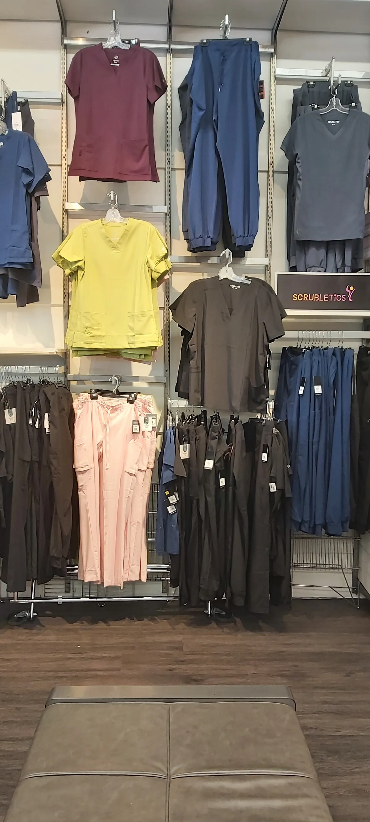 A scrubs wall with tops and joggers in burgundy, blue, yellow, charcoal and pink